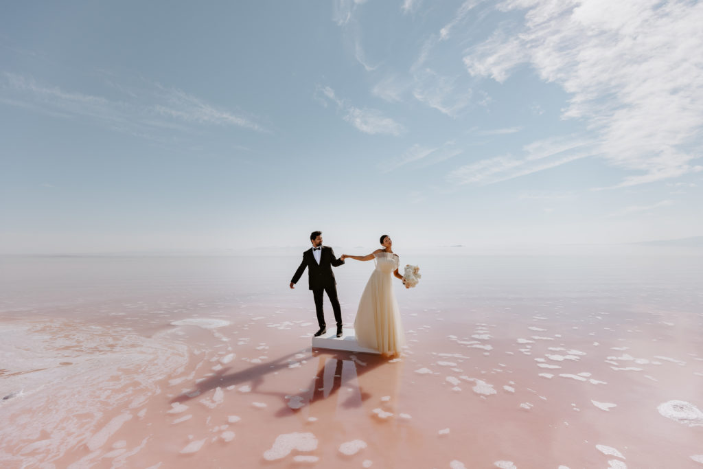 wide image of the couple holding hands in the pink lake 