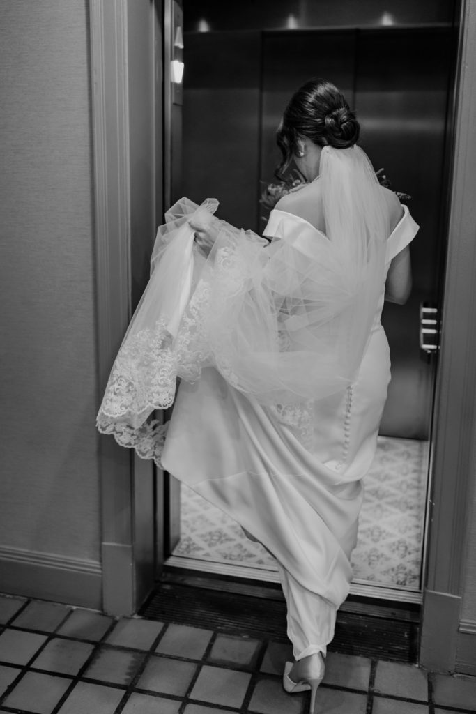 Bride is going into the elevator holding her wedding dress 